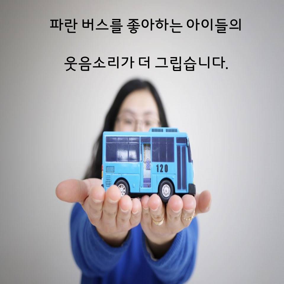 배경 : 직원이 파란 옷을 입고 파란버스 장난감을 들고 있다. 설명글 : 파란 버스를 좋아하는 아이들의 웃음소리가 더 그립습니다.